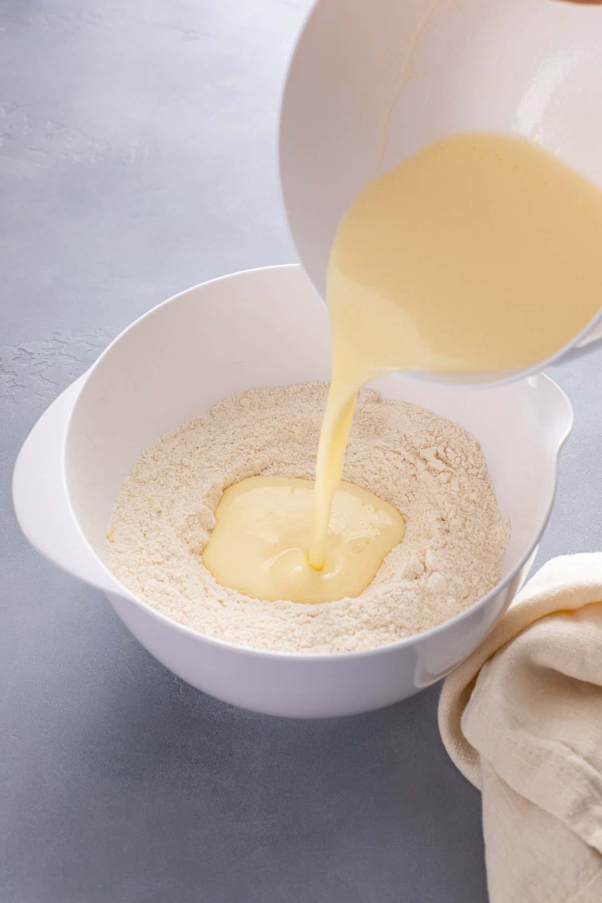 Wet ingredients for muffin batter being poured into a bowl of the dry ingredients.