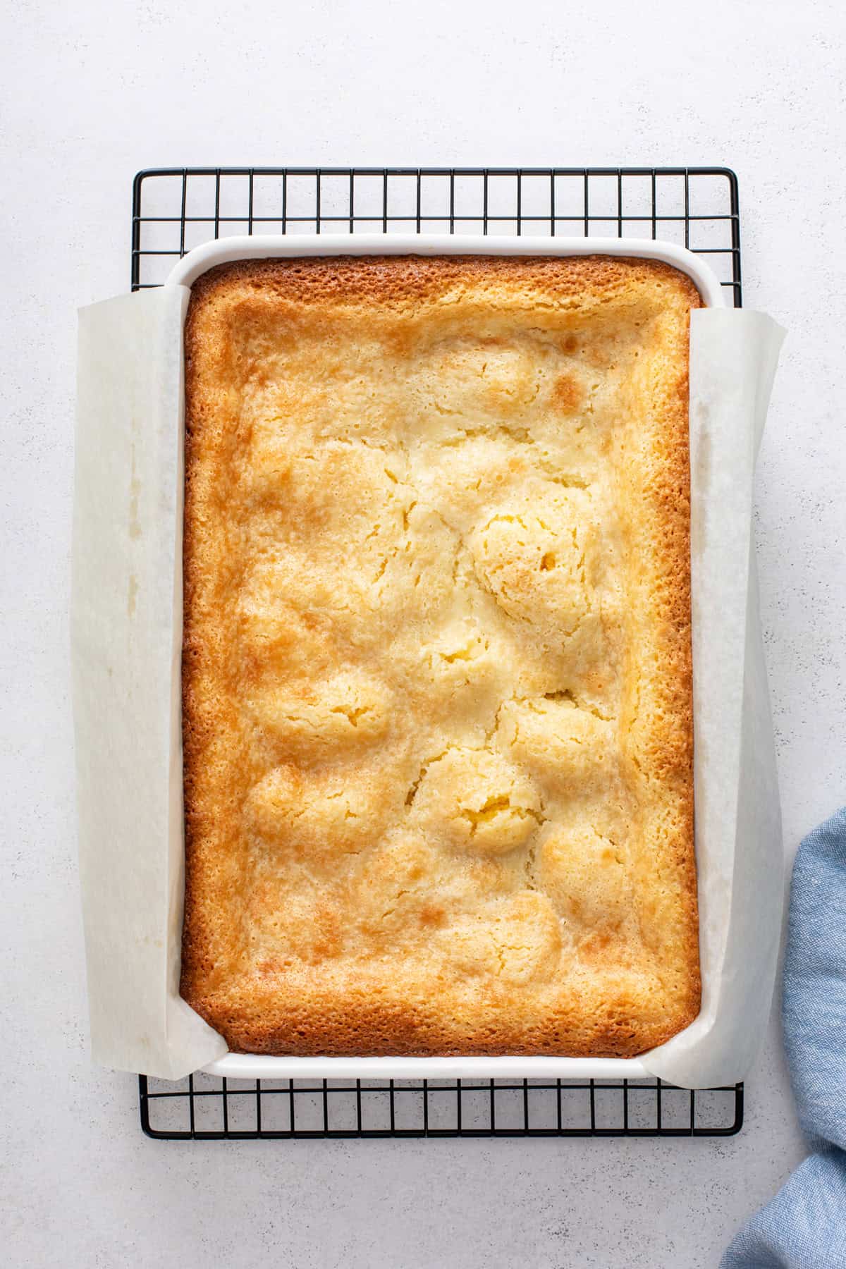 Baked lemon gooey butter cake in a white pan cooling on a wire rack.