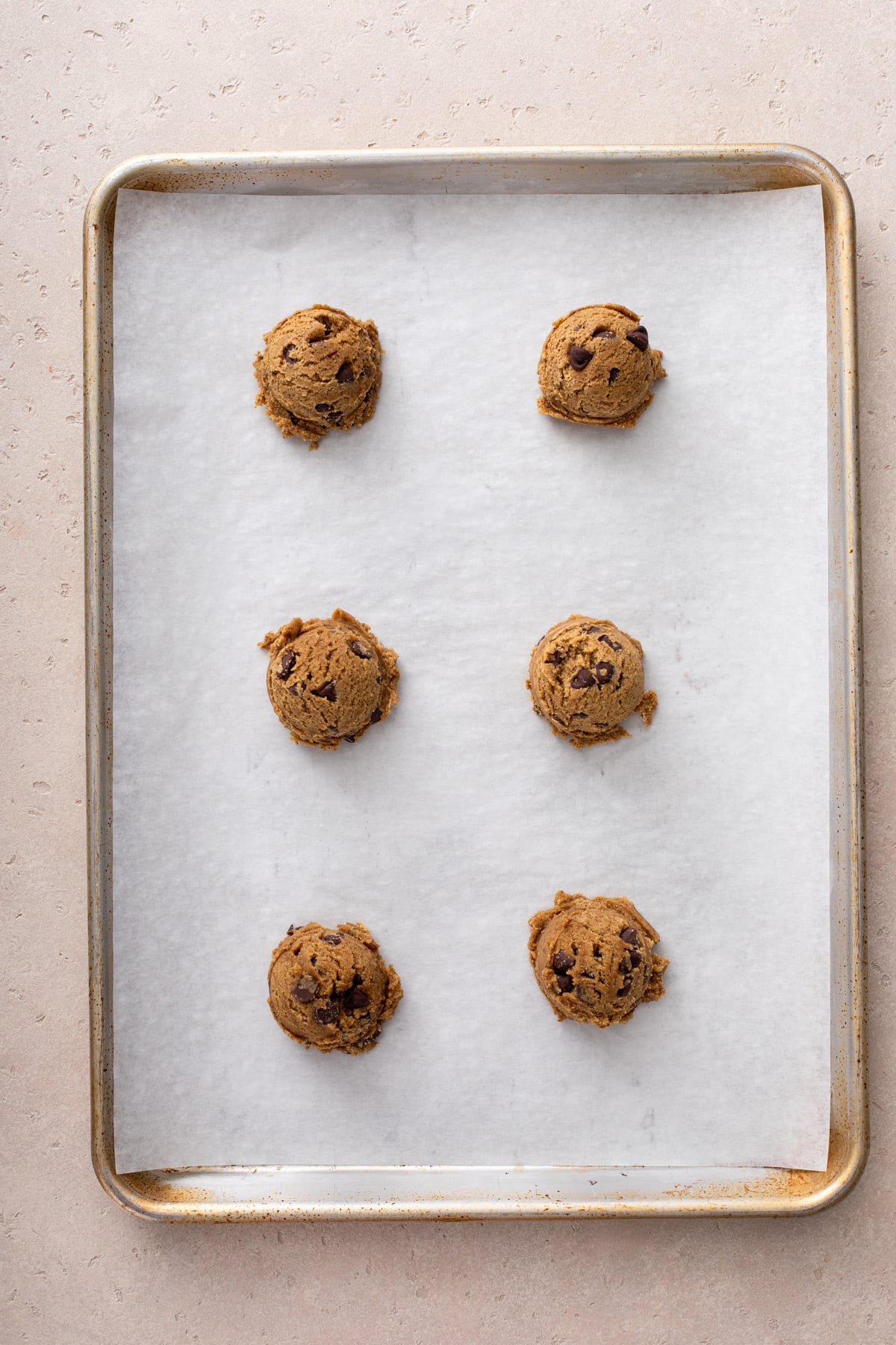 6 balls of espresso chocolate chip cookie dough set on a lined sheet pan, ready to go in the oven.
